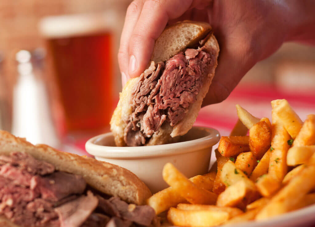 steak sandwich being dipped into sauce  with a side of fries